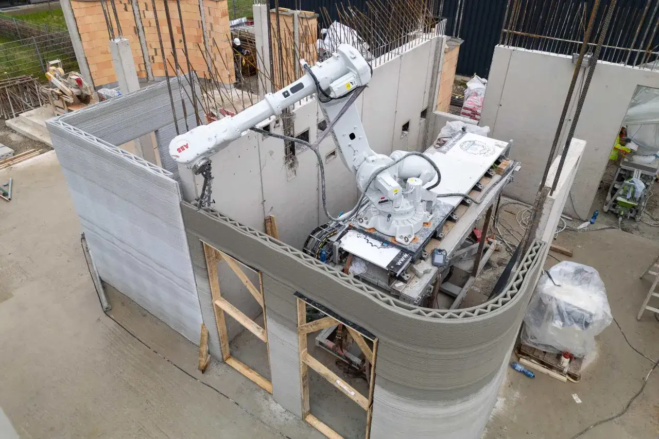 Ein Roboterarm druckt die W&auml;nde eines 3D-Druck-Hauses. Die Schichten aus Beton sind deutlich sichtbar.