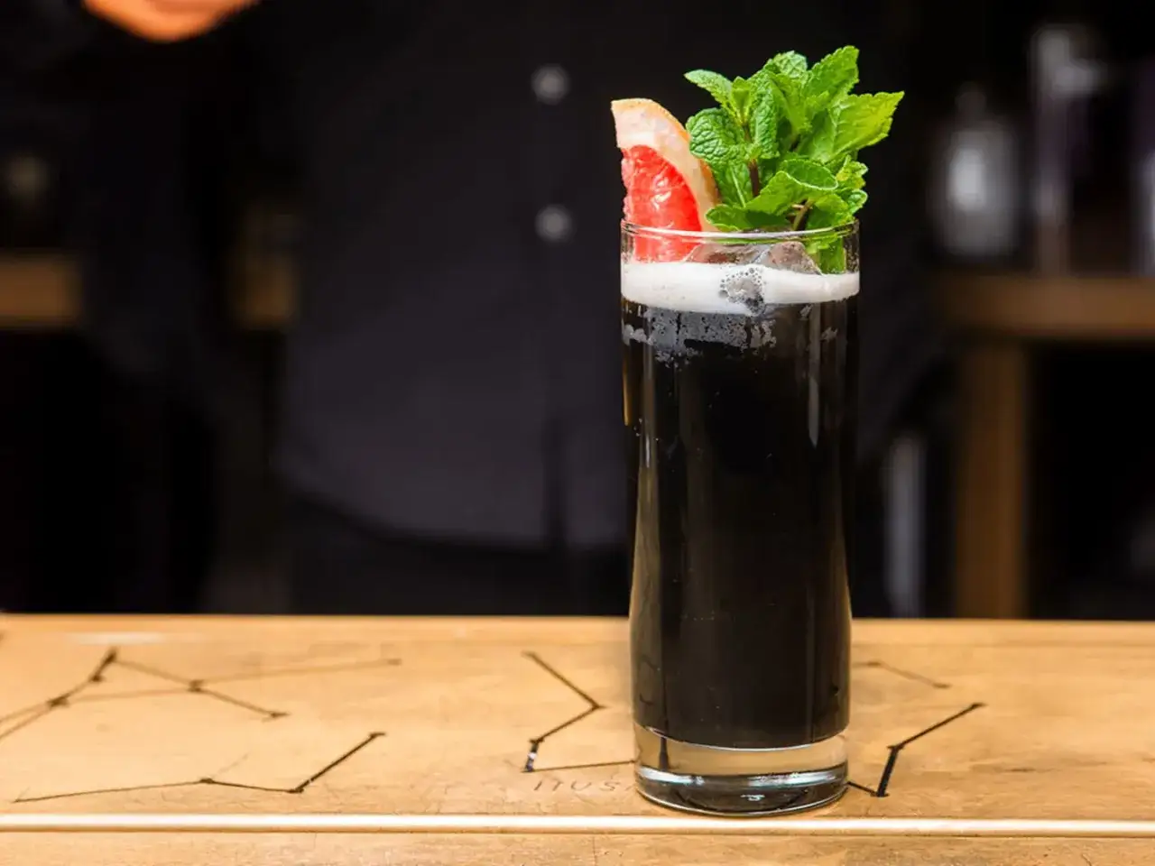 En h&ouml;g, elegant glas med en m&ouml;rk, svart drink. Garnerad med en grapefruktklyfta och f&auml;rsk mynta.