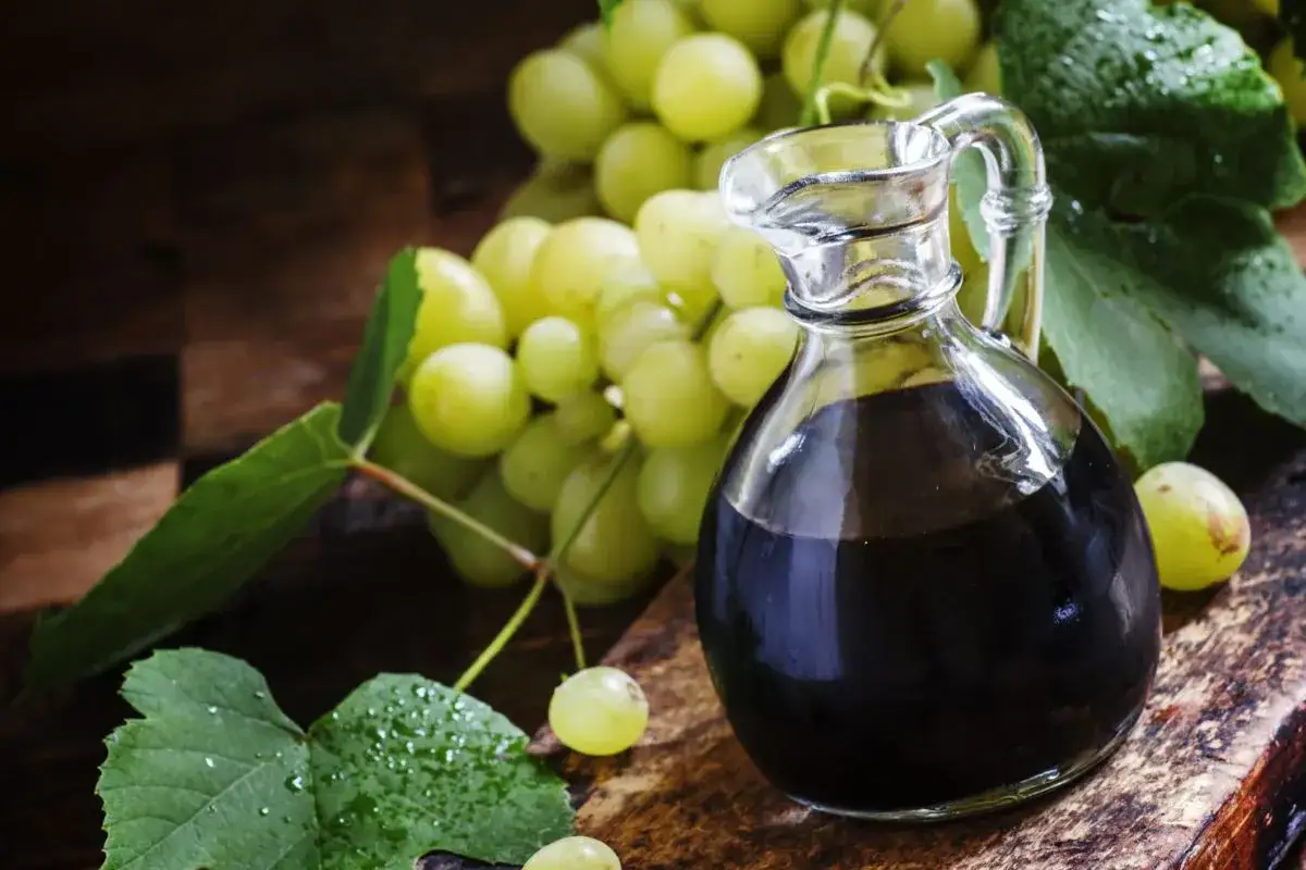 Szukasz pomysłów, czym zastąpić ocet balsamiczny? Na zdjęciu ciemny płyn w karafce i kiść zielonych winogron.