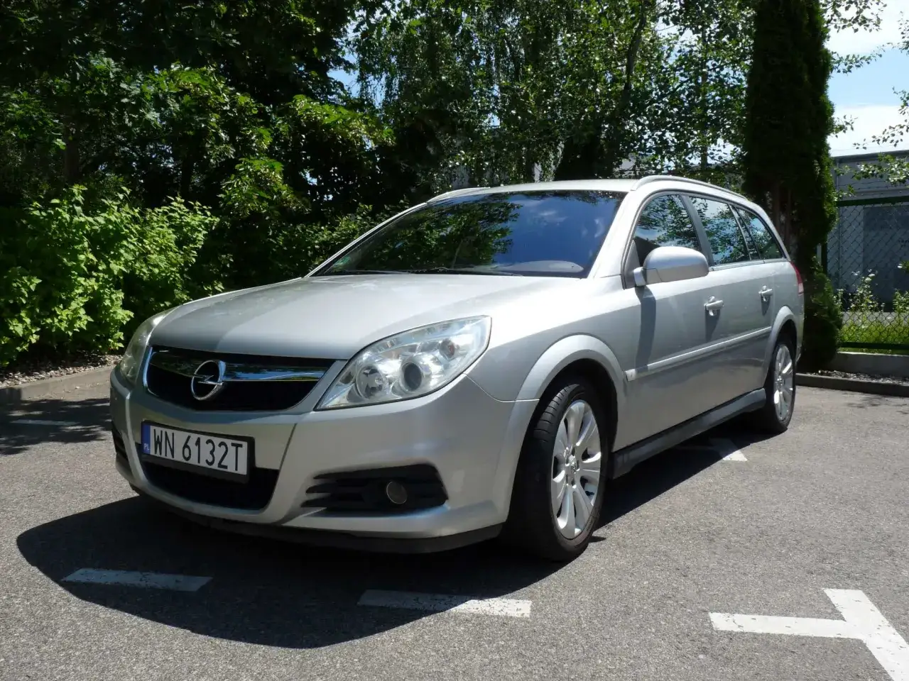 Srebrny Opel Vectra kombi zaparkowany na zewnątrz, otoczony zielenią.