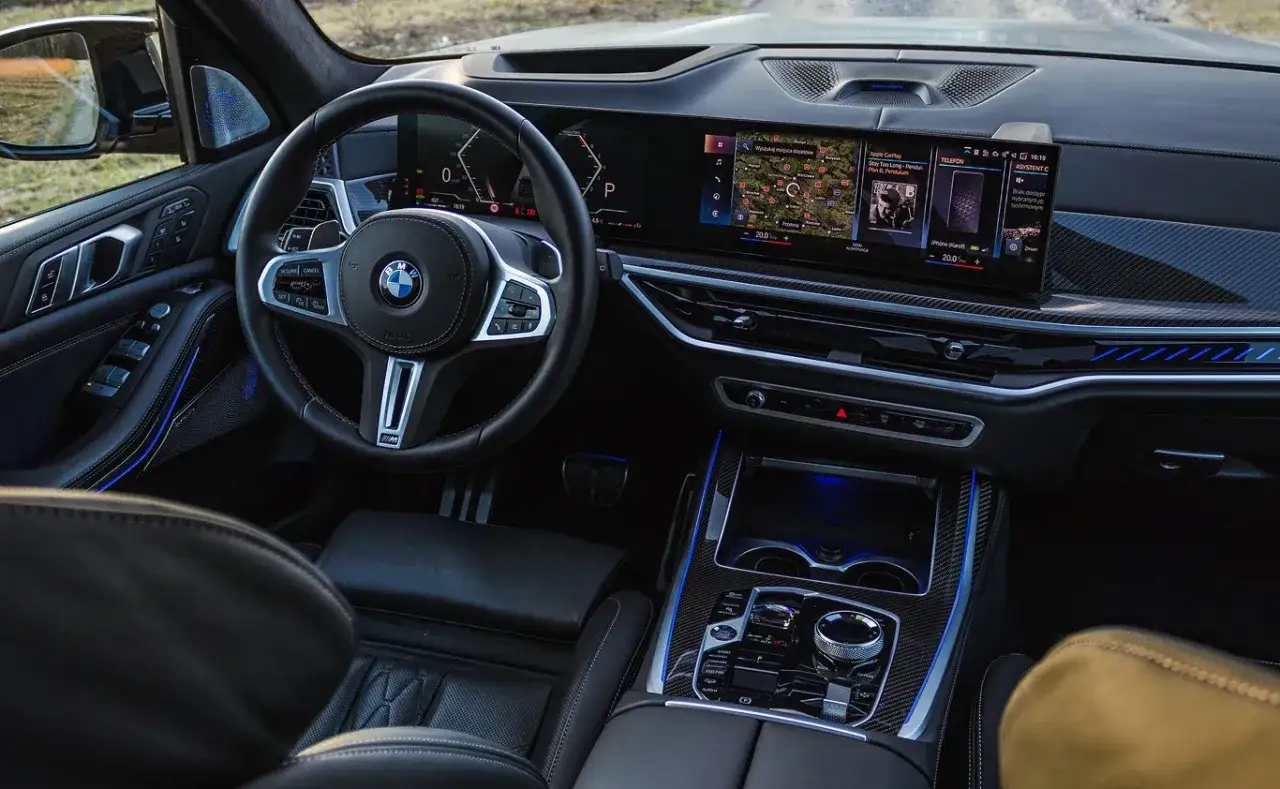 Wnętrze BMW X7 M60i z dużym ekranem multimediów, cyfrowymi zegarami i sportową kierownicą.
