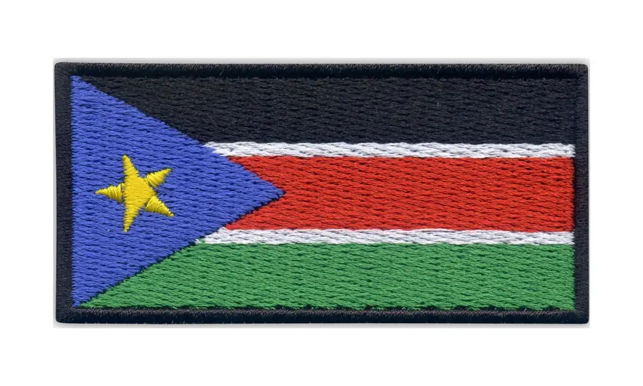 Naszywka z flagą Sudanu Południowego. Czarny pas na górze, pod nim biały, czerwony i zielony pas. Po lewej niebieski trójkąt z żółtą gwiazdą.