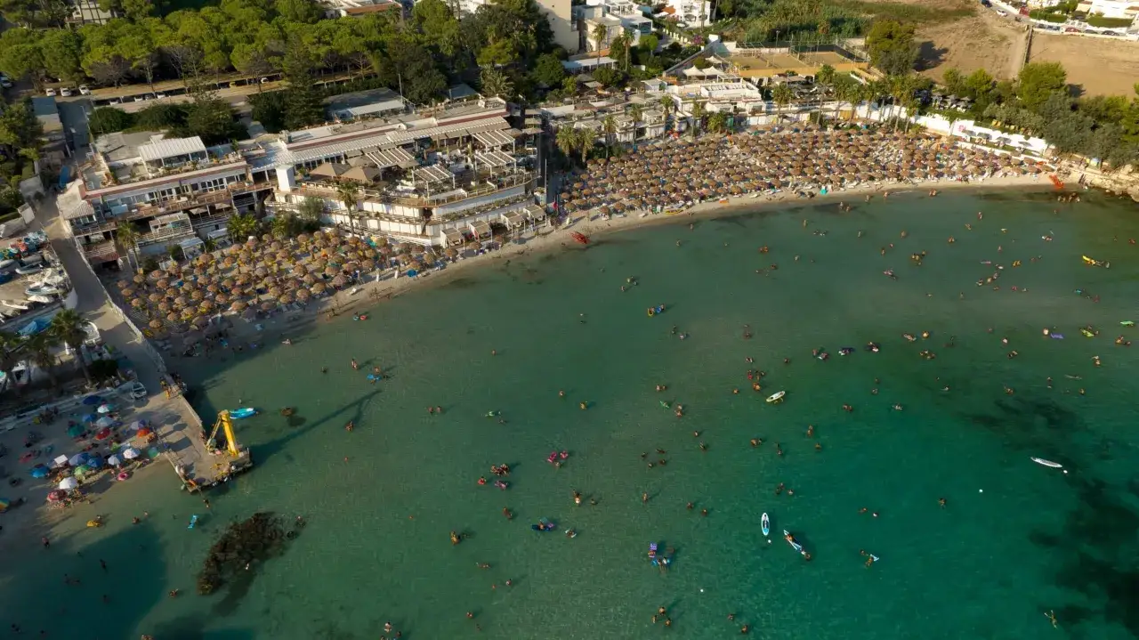 Vista aerea di una spiaggia affollata con ombrelloni e persone che nuotano nel mare cristallino. Una delle spiagge pi&ugrave; belle del mare di Taranto.