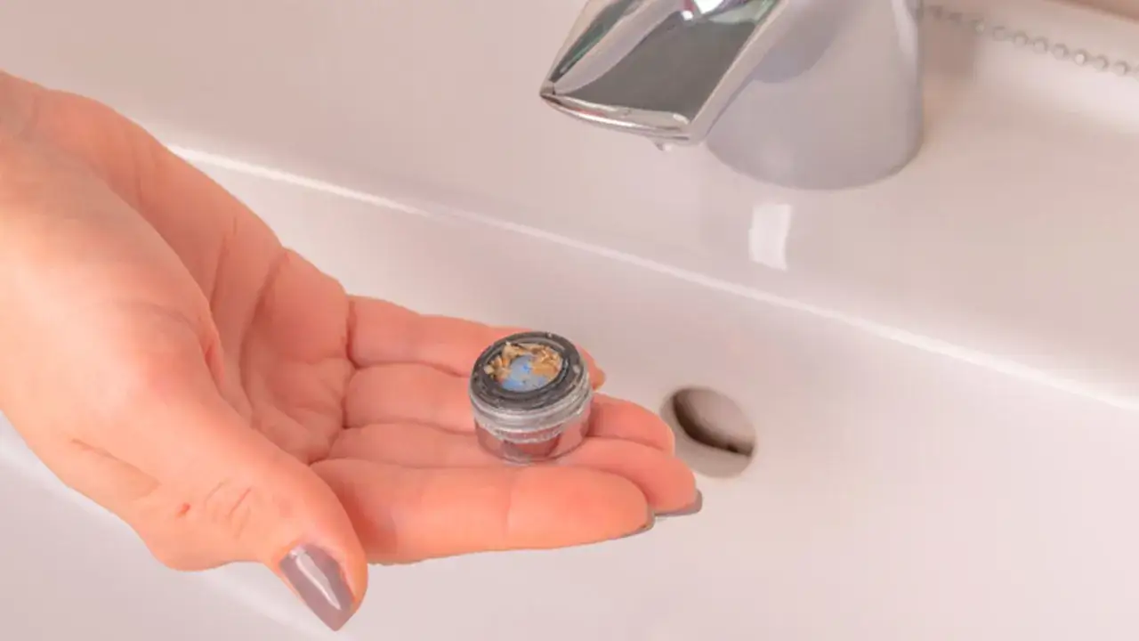 Mano che mostra un aeratore del rubinetto bloccato dal calcare, un passo fondamentale per capire come sbloccare un rubinetto bloccato dal calcare.