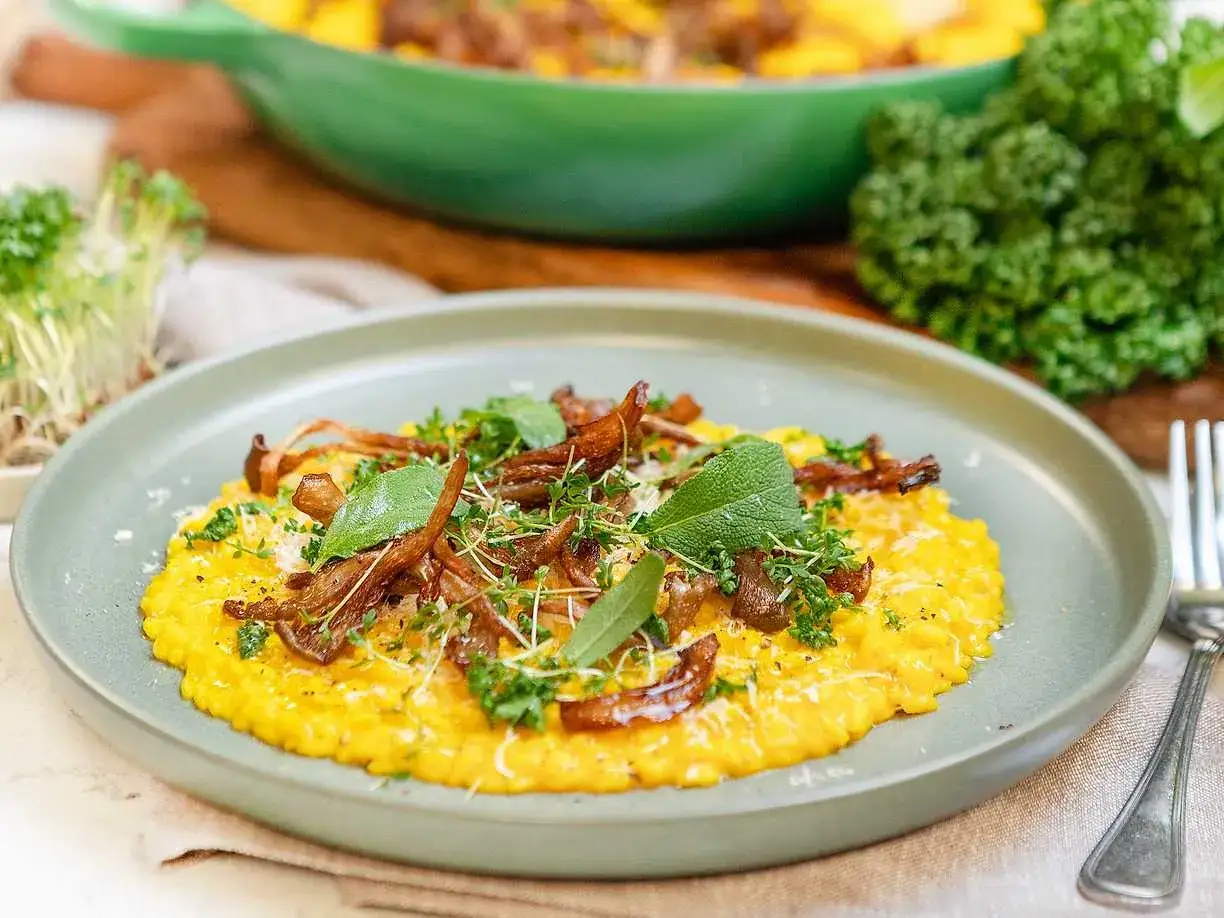 En krämig risotto alla milanese med svamp och örter, serverad på en ljusgrön tallrik.