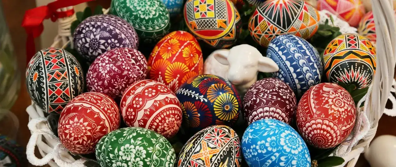 Kosz pełen barwnych pisanek i ceramiczna owieczka. Tradycje wielkanocne w całej okazałości, zachwycające wzory i kolory.