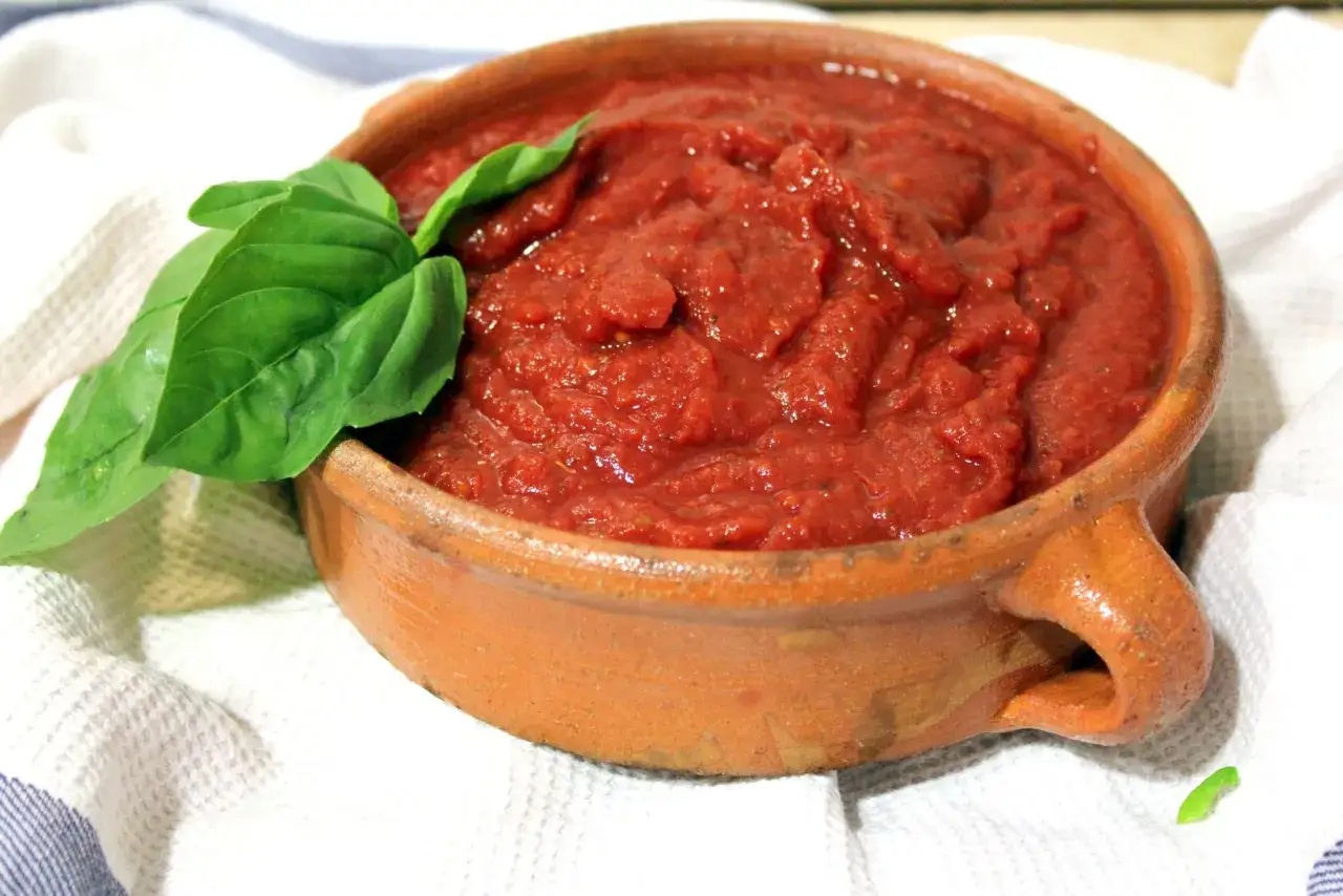 Salsa para pizza casera en cuenco de barro, decorada con hojas de albahaca fresca. ¡Lista para tu próxima creación!