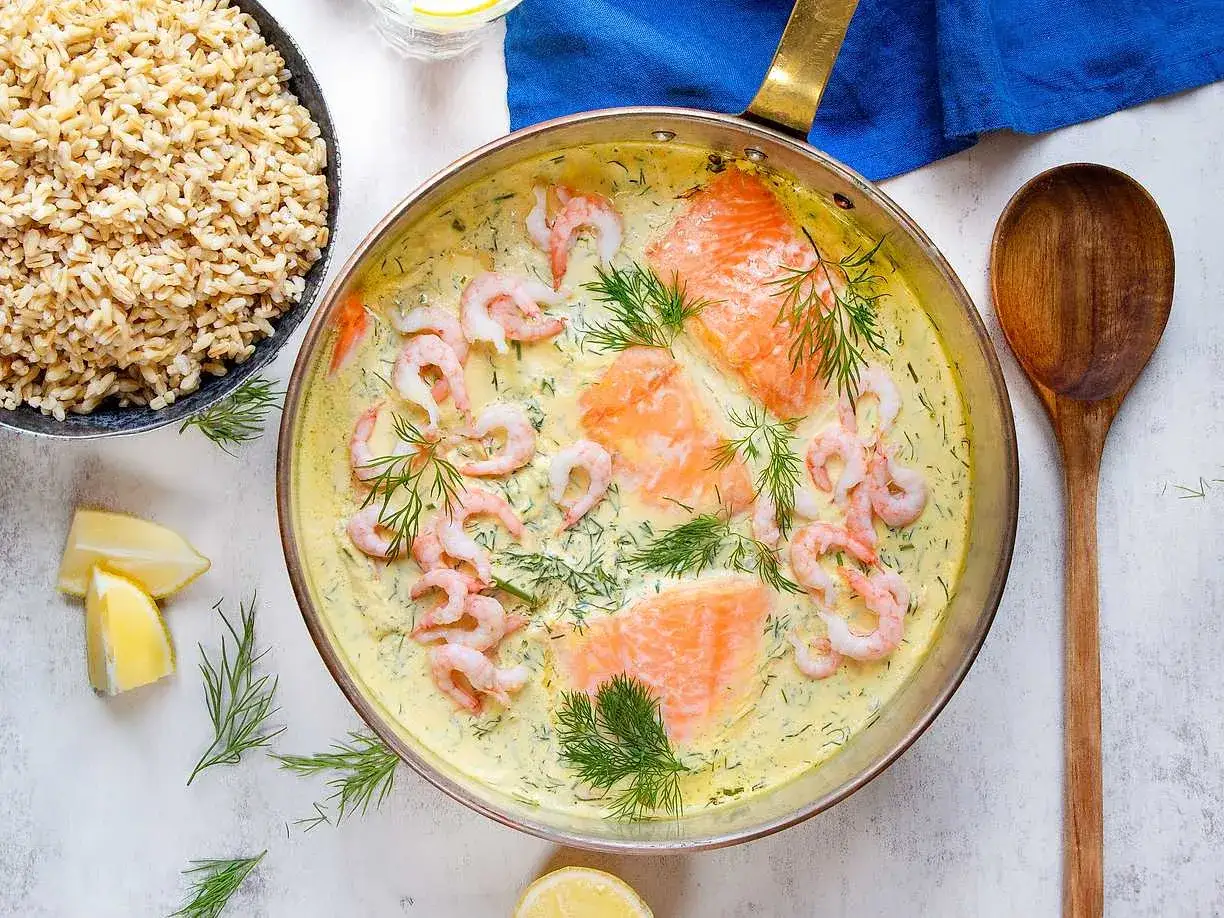 Laxfiléer och räkor i en krämig sås till lax, garnerad med dill och citronklyftor. Serveras med fullkornsris.