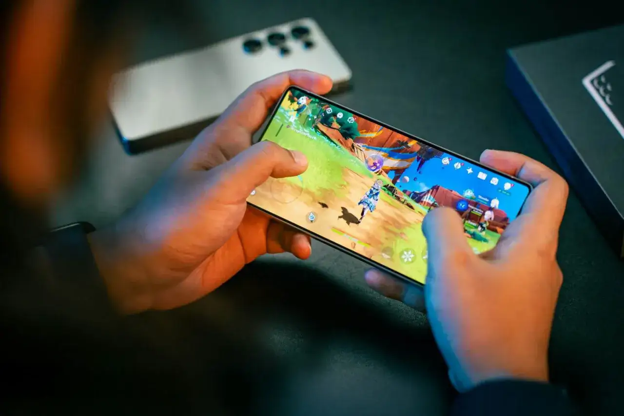 Ręce trzymają smartfon, na którym widać kolorową grę. To idealny sposób na zabicie nudy, gdy masz ochotę na gry na telefon.