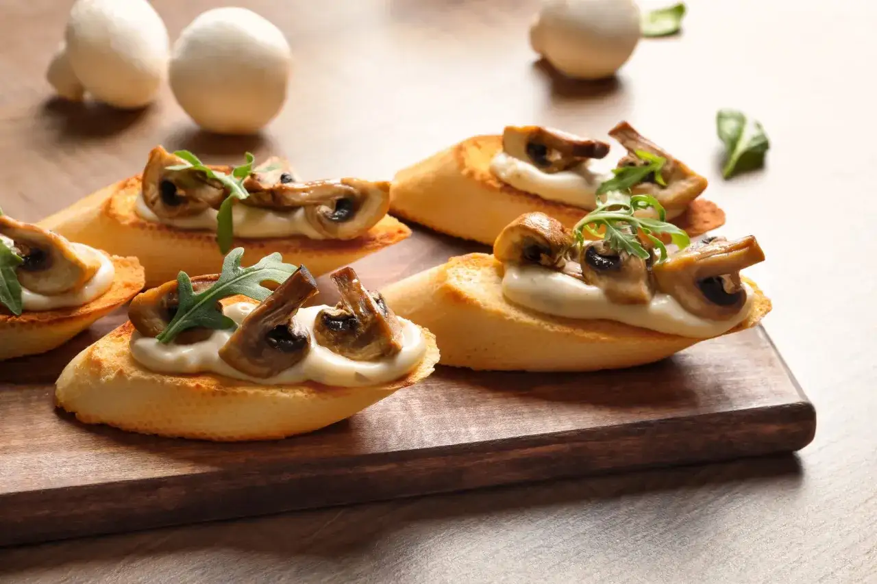 Pyszna bruschetta z pieczarkami, podana na chrupiącej bagietce z kremowym sosem i rukolą. Idealna na przekąskę.