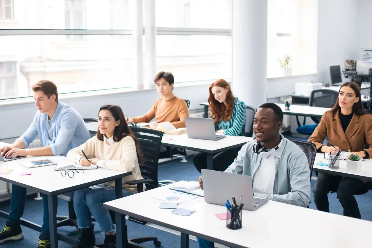 Des étudiants en salle de classe, certains travaillent sur leurs ordinateurs portables. Ils semblent suivre un cours sur le **master finance quantitative classement**.