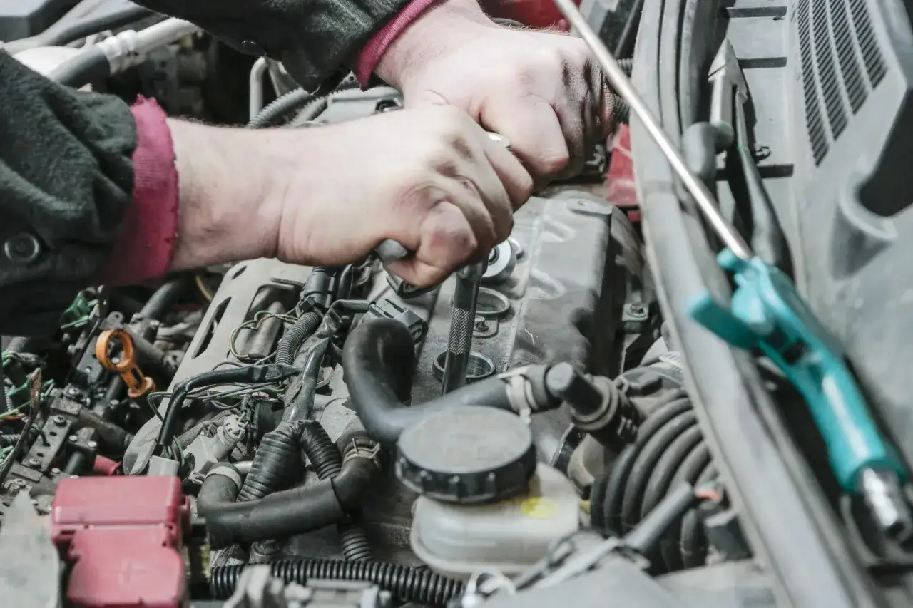 Mechanik dokonuje wymiany świec zapłonowych, używając klucza nasadowego do odkręcenia jednej z nich.