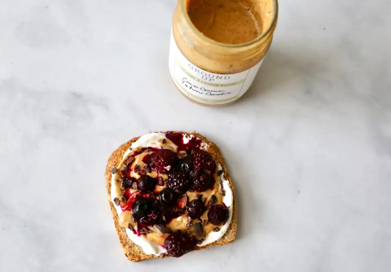 Tartine de pain grillé avec une crème onctueuse, des baies et des éclats de cacao. Un pot de beurre de sésame et de cajou, une excellente alternative par quoi remplacer le beurre de cacahuète.