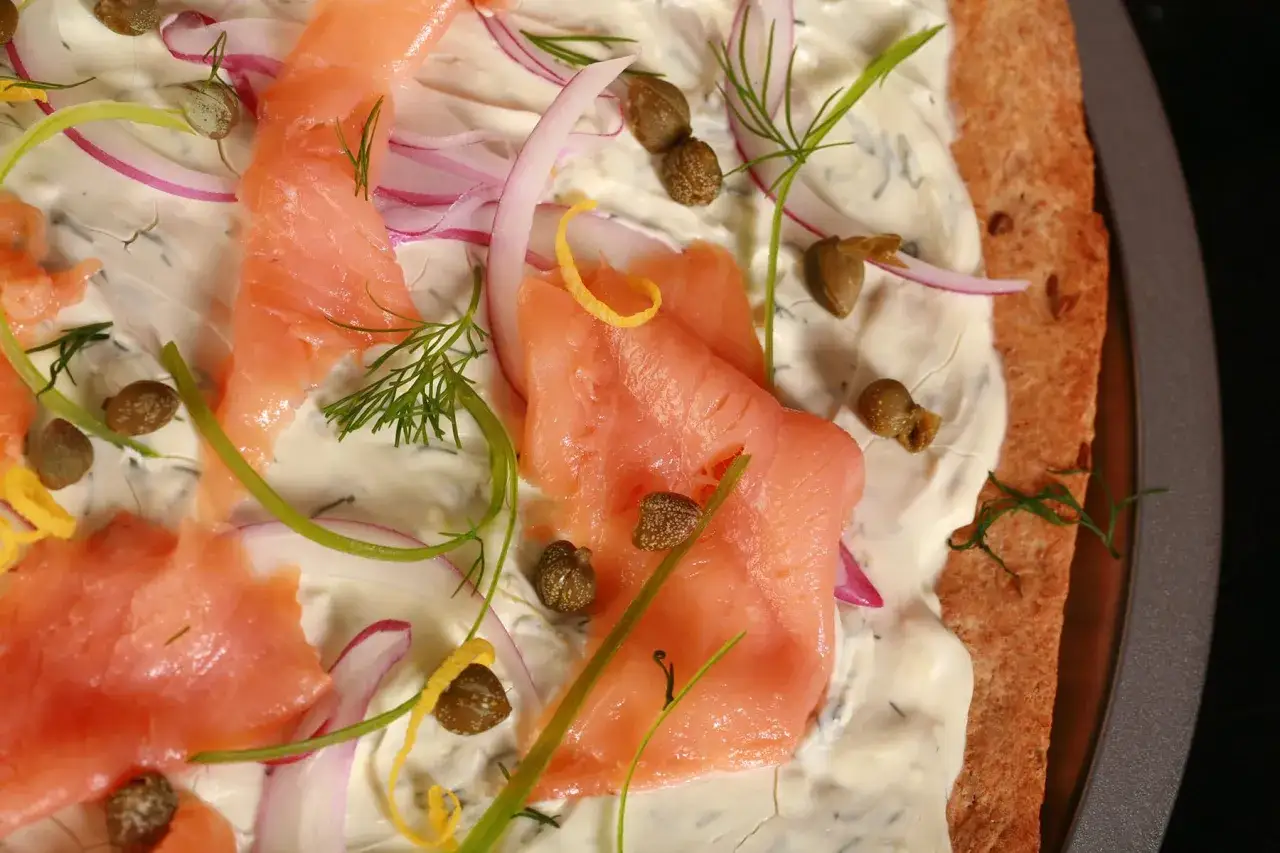 Délicieuse pizza saumon, garnie de crème, oignons rouges, câpres et aneth. Un délice frais et savoureux.