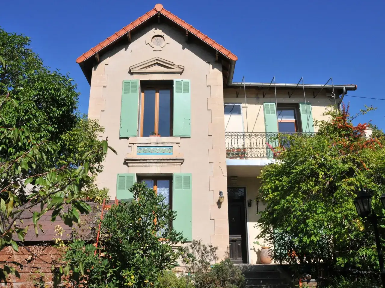Belle bâtisse avec volets verts, idéale pour une auberge de jeunesse en Camargue. Le soleil brille sur les arbres luxuriants.