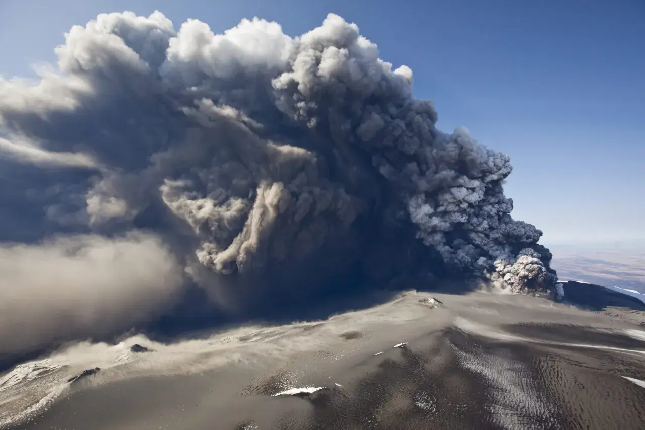 Potężna erupcja wulkanu wyrzuca kłęby dymu i popiołu na tle błękitnego nieba. Wygląda jak katastrofa z roku 536.