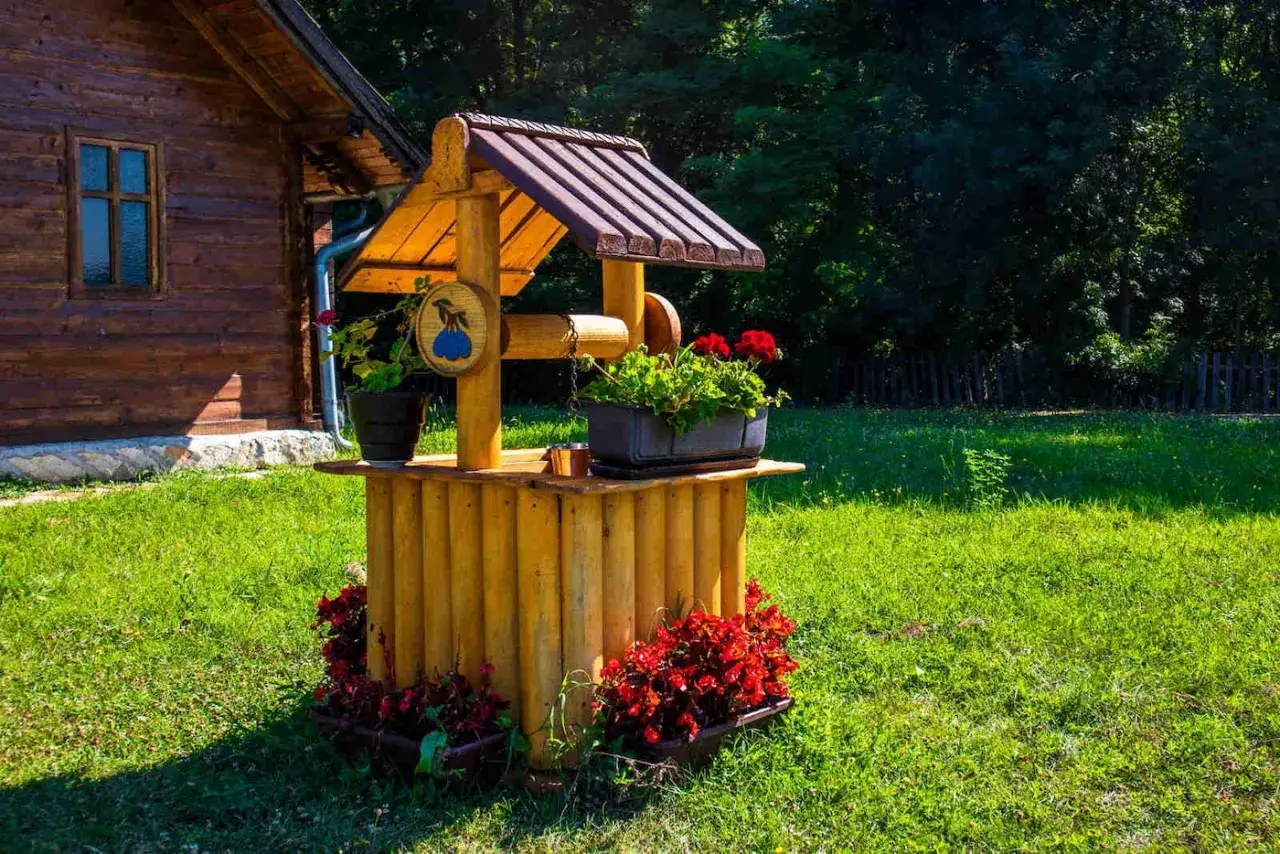 Drewniana studnia ozdobiona kwiatami, idealna do ogrodu. Pytanie, czym obłożyć studnię, rozwiązane przez naturalne drewno i zieleń.