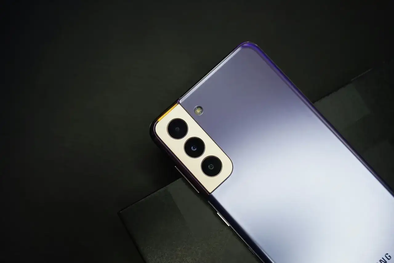 Fioletowy Samsung S21, rok produkcji 2021, z potr&oacute;jnym aparatem i złotą ramką, leży na czarnym tle.