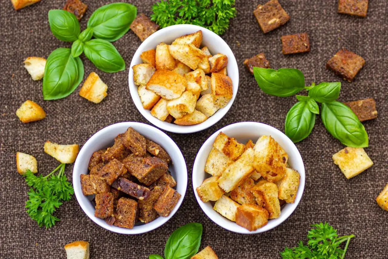 Drei Schalen mit selbstgemachten Croutons, garniert mit Basilikum und Petersilie. Perfekt f&uuml;r Salate oder Suppen!