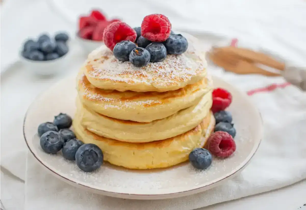 Pile de pancakes sans gluten, garnie de framboises et myrtilles fra&icirc;ches, saupoudr&eacute;e de sucre glace.