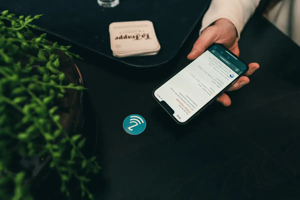 En hand håller en nfc mobil över en rund symbol. Mobilen visar en meny med maträtter.