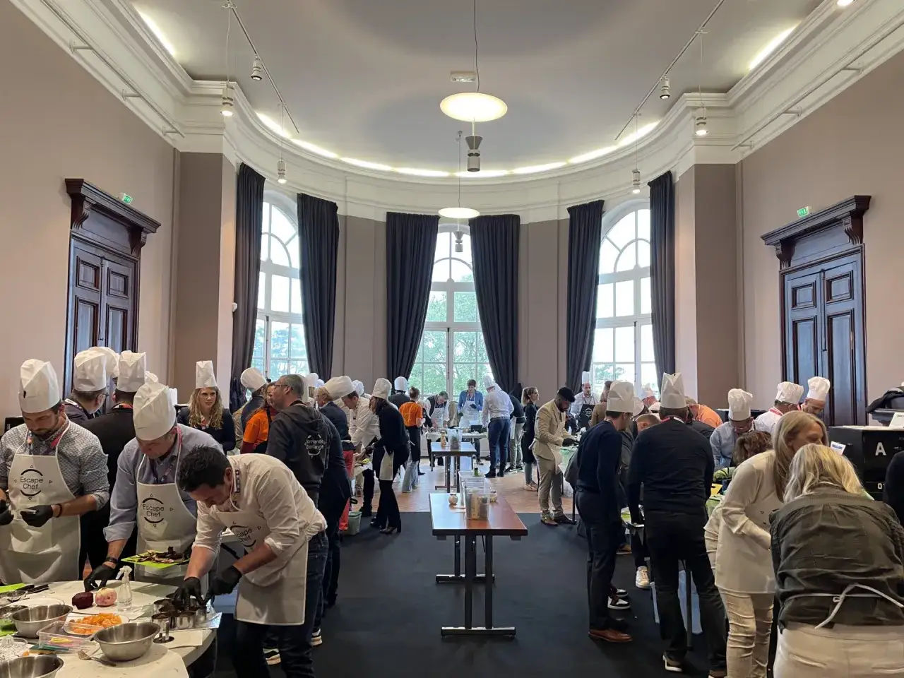 Une activité séminaire entreprise où des participants, coiffés de toques de chef, s'initient à la cuisine dans une grande salle lumineuse.