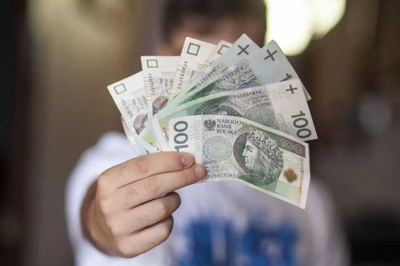 Dłoń trzyma polskie banknoty. Czy można płacić sklejonym banknotem? To pytanie nurtuje wielu.