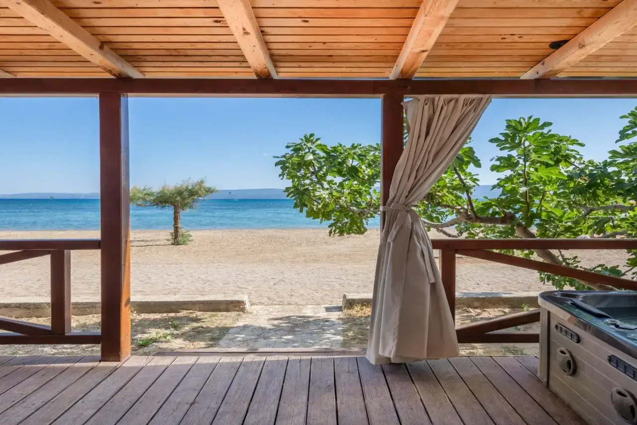 Widok z tarasu na plażę i morze. Na pierwszym planie drewniana podłoga i balustrada. W rogu widać jacuzzi. To idealne miejsce na relaks w camp galeb.