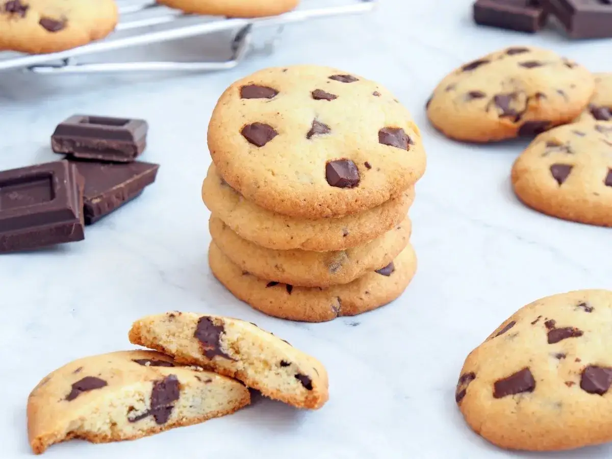 Galletas de chocolate recién horneadas, perfectas para tu próxima receta de galletas chocolate. Trozos de chocolate negro y una rejilla de enfriamiento al fondo.