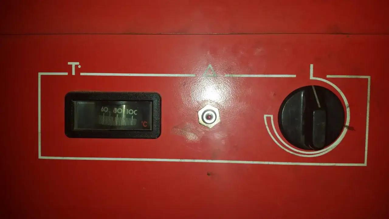 Panneau rouge d'une chaudière fioul. Thermomètre affichant 70°C, un bouton rotatif et un voyant. La chaudière fioul démarre puis s'arrête.