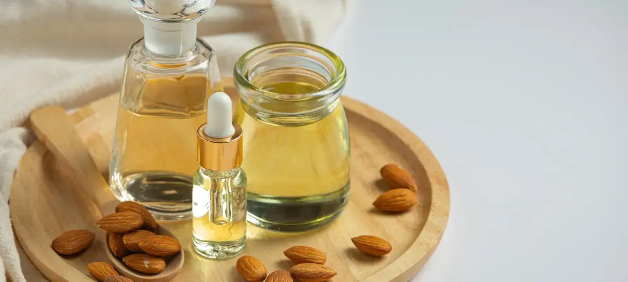 Aceite de almendras en frascos y cuchara de madera, con almendras enteras. El aceite de almendras mancha la piel con el sol, pero nutre.