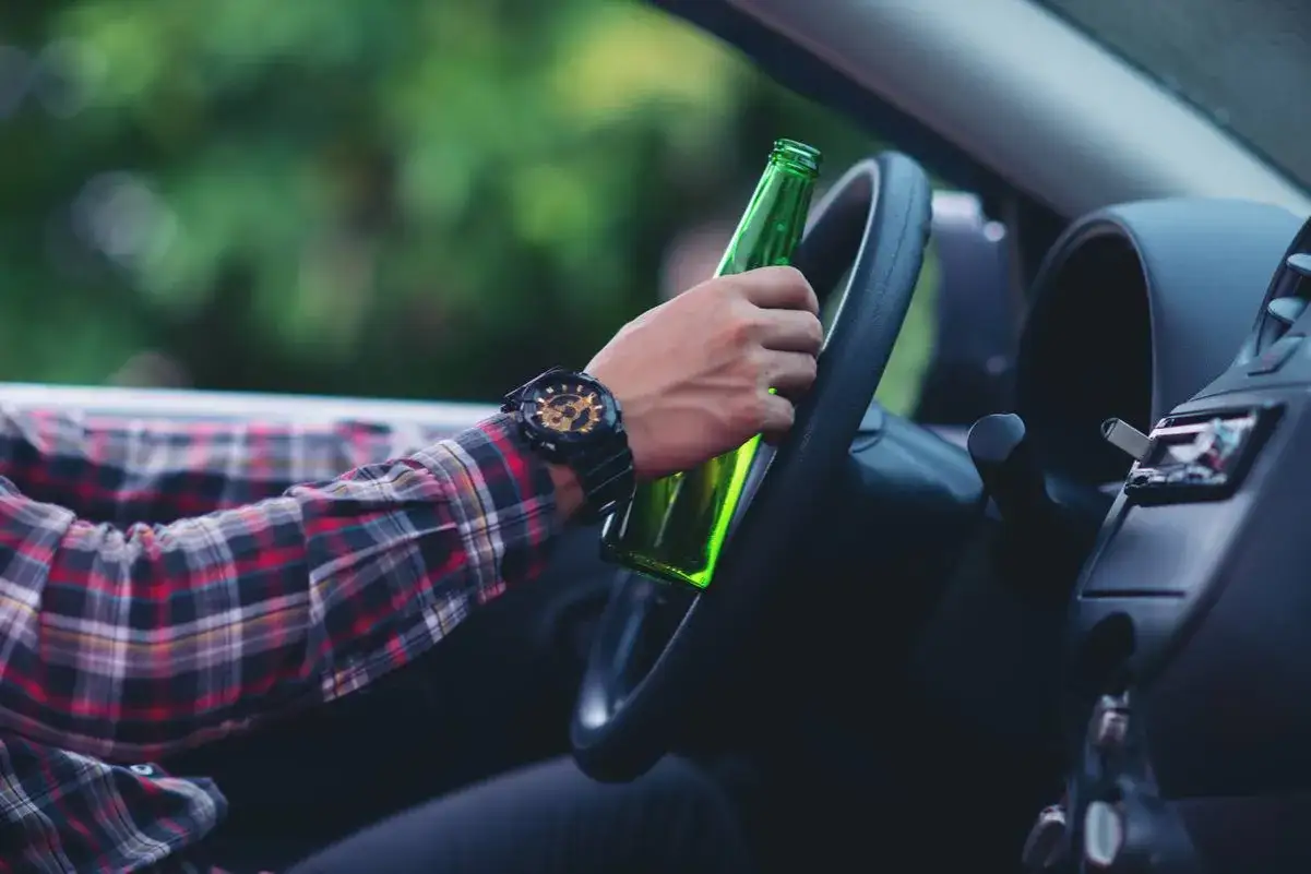 Mężczyzna w kratę trzyma butelkę piwa za kierownicą. Zastanawia się, ile promili w Austrii można mieć, prowadząc auto.