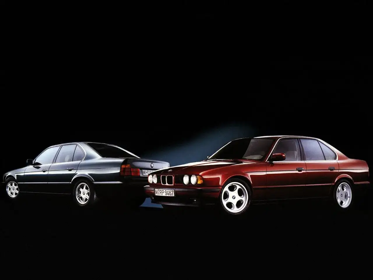 Dwa klasyczne BMW E34, jeden ciemny, drugi bordowy, prezentują swoje eleganckie linie na czarnym tle.