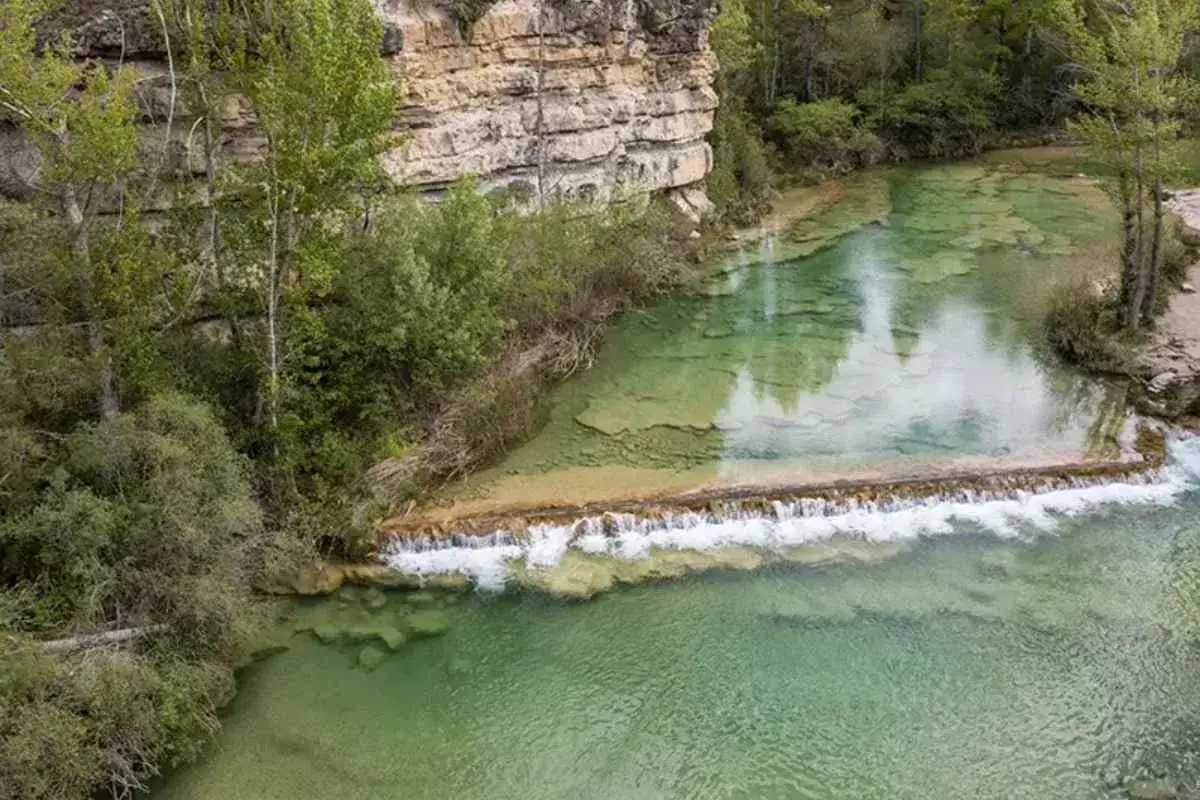 Agua turquesa en el embalse de Guadalajara, con cascadas y acantilados rocosos rodeados de vegetaci&oacute;n exuberante.