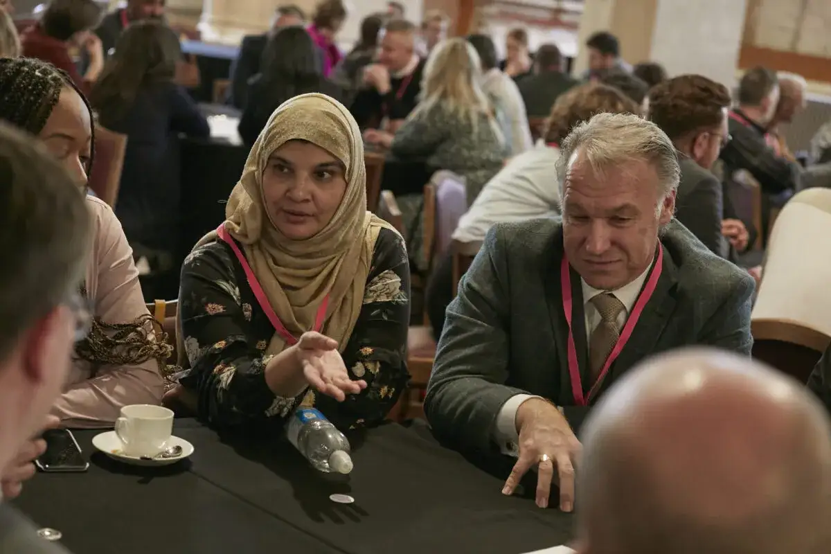 A woman in a hijab and a man in a suit discuss at a table, illustrating why does inclusion matter in fostering diverse perspectives and understanding.