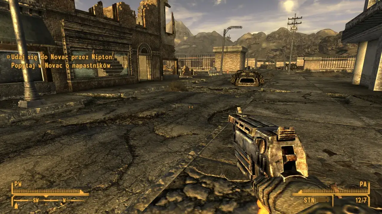 Pustynny krajobraz z ruiny miasta, gracz trzyma broń. W rogu ekranu widać tekst misji z gry Fallout: New Vegas, sugerujący polskie spolszczenie.