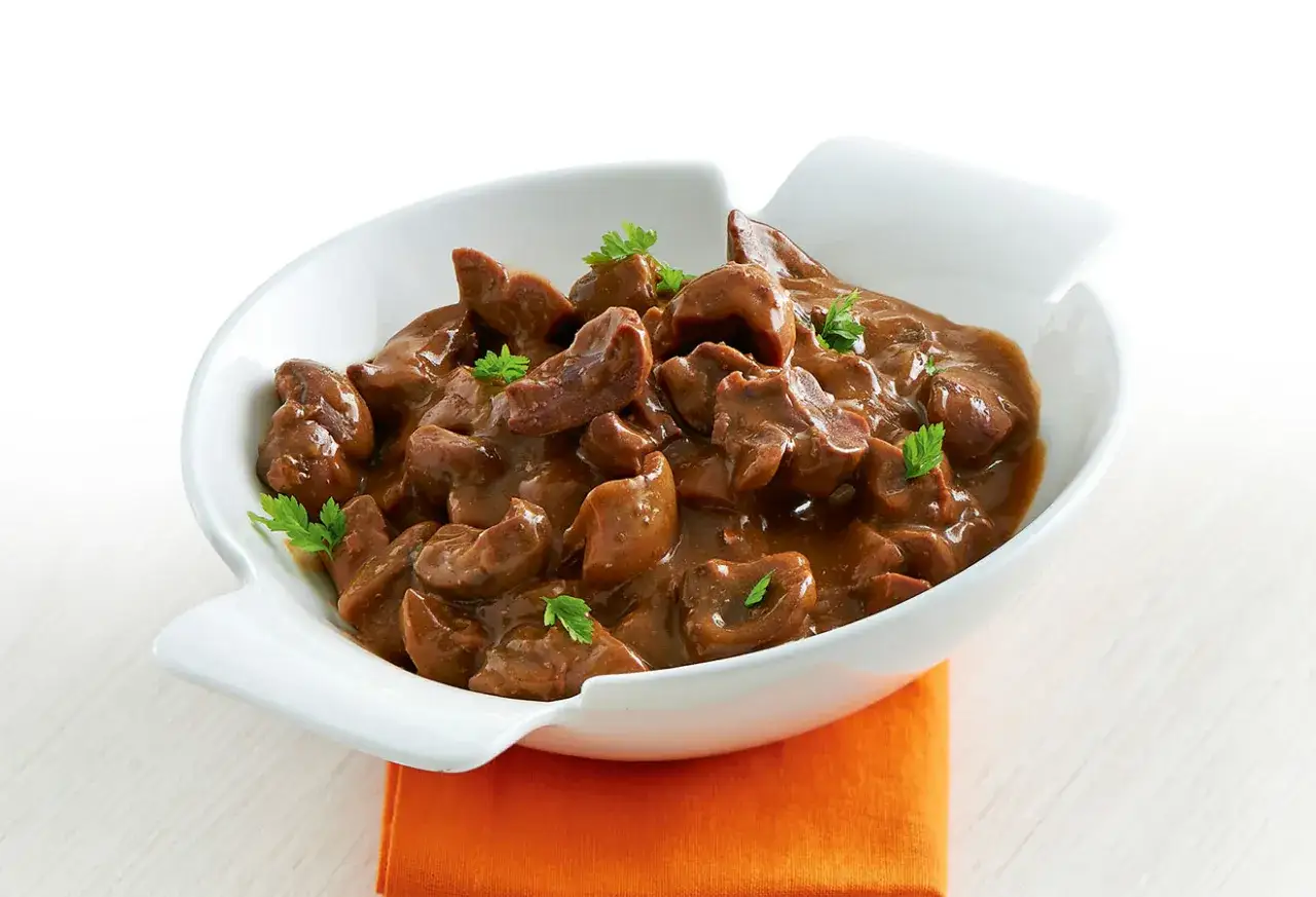Un plat de rognons sauce madère, tendres et savoureux, servis dans un bol blanc avec une touche de persil frais.
