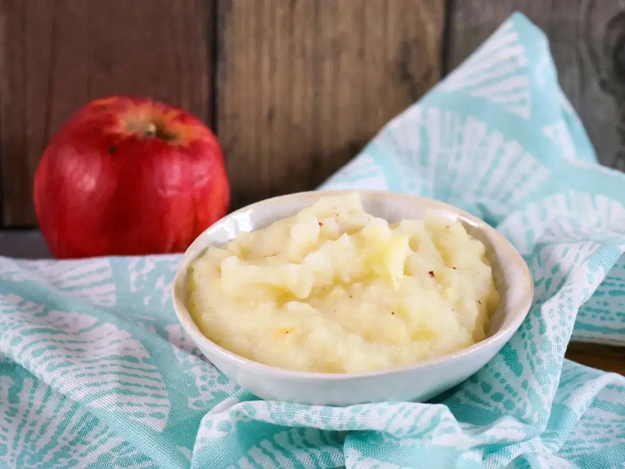 Sch&uuml;ssel mit cremigem Apfelmus, perfekt als obstbrei baby. Daneben ein frischer roter Apfel.
