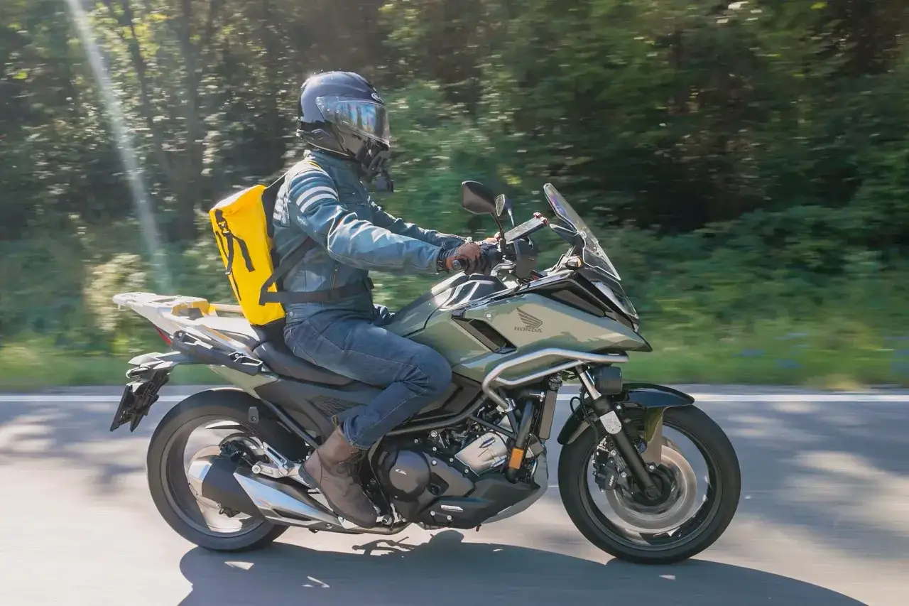 Fahrer auf einem grünen Honda Automatik Motorrad mit gelber Tasche fährt durch sonnigen Wald.