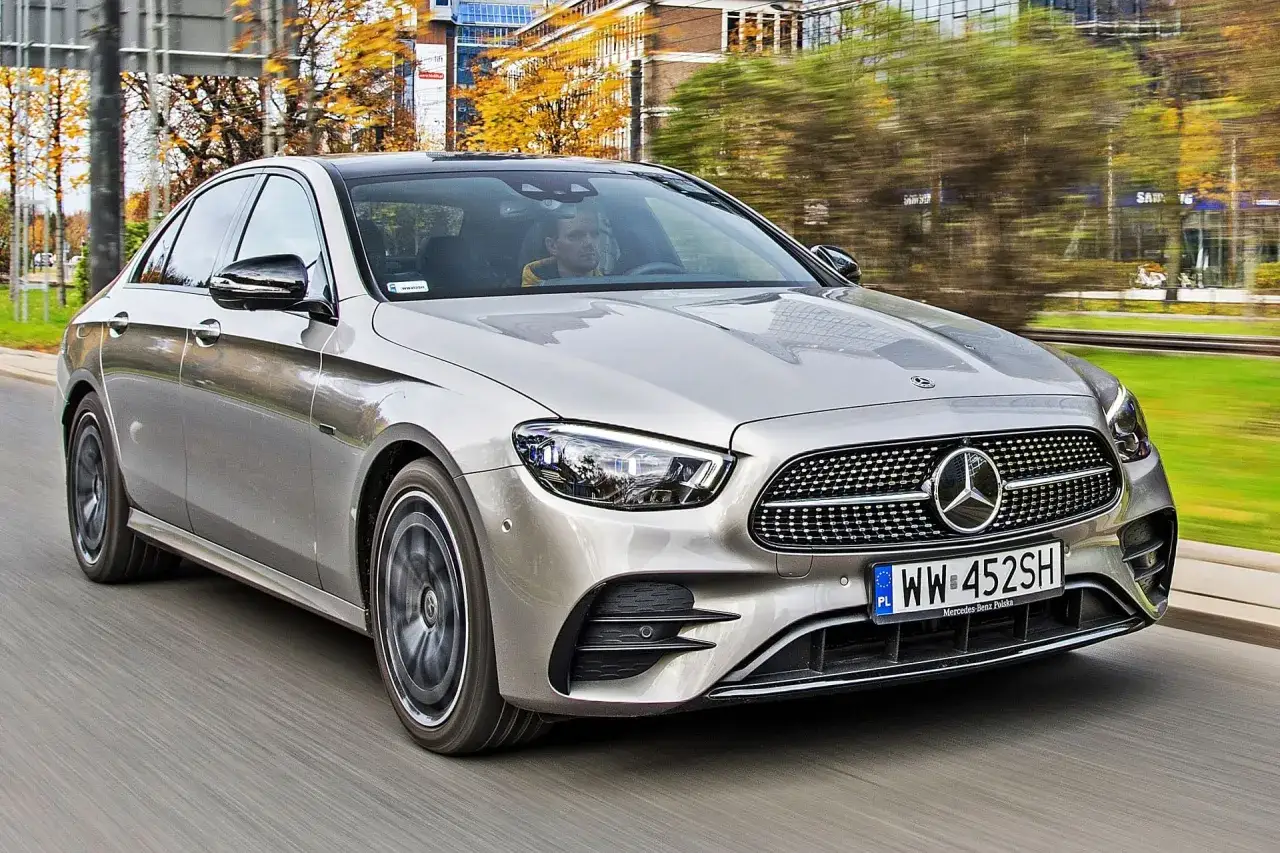 Srebrny Mercedes-Benz E-Class w ruchu miejskim, z kierowcą za kierownicą.