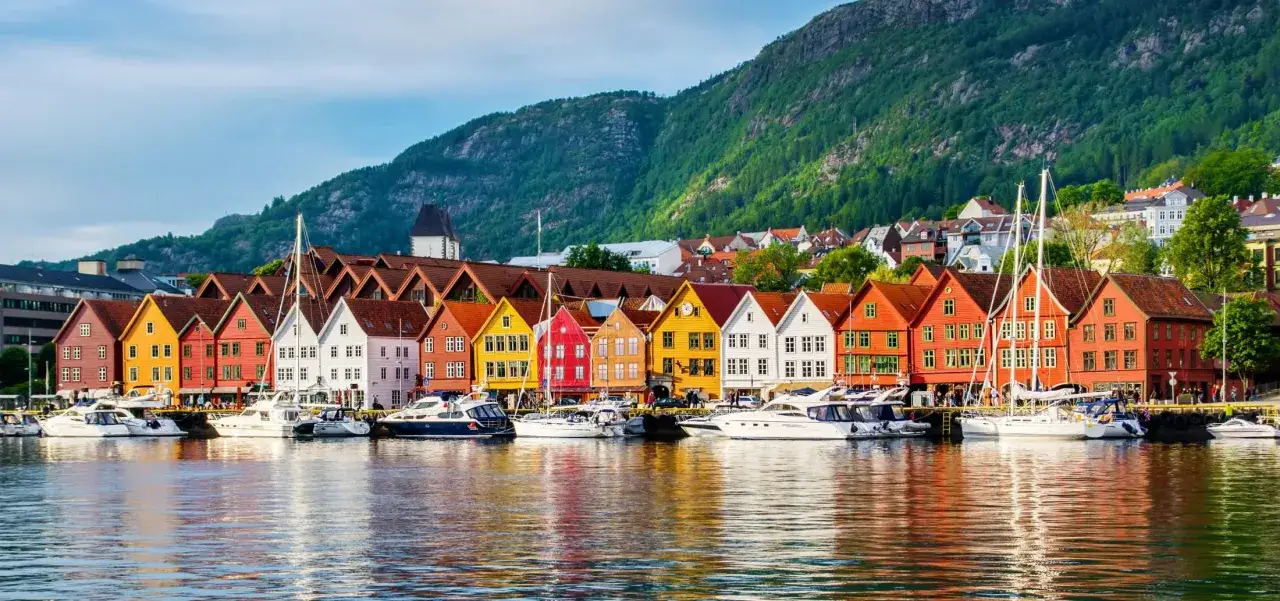 Kolorowe kamienice Bryggen, wpisane na listę UNESCO, to obowiązkowy punkt, co zwiedzić w Bergen. W tle zielone wzgórza i łodzie.