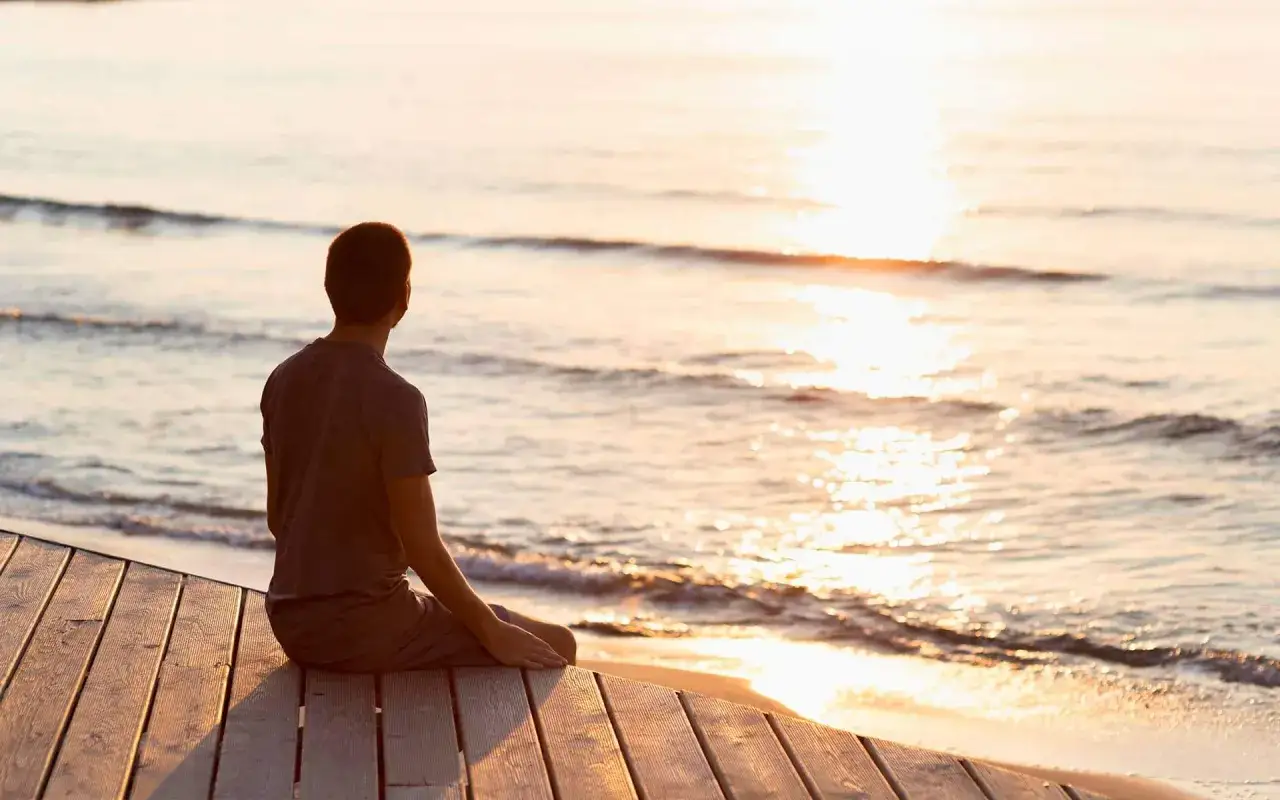 A person sits on a wooden pier, gazing at the sunlit ocean waves. This peaceful moment is what would make today great.