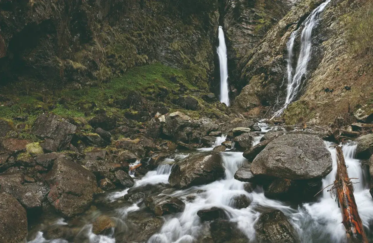La cascade de Luchon dévale une paroi rocheuse, son eau blanche se mêlant aux rochers et à la mousse verdoyante. Un spectacle naturel saisissant.