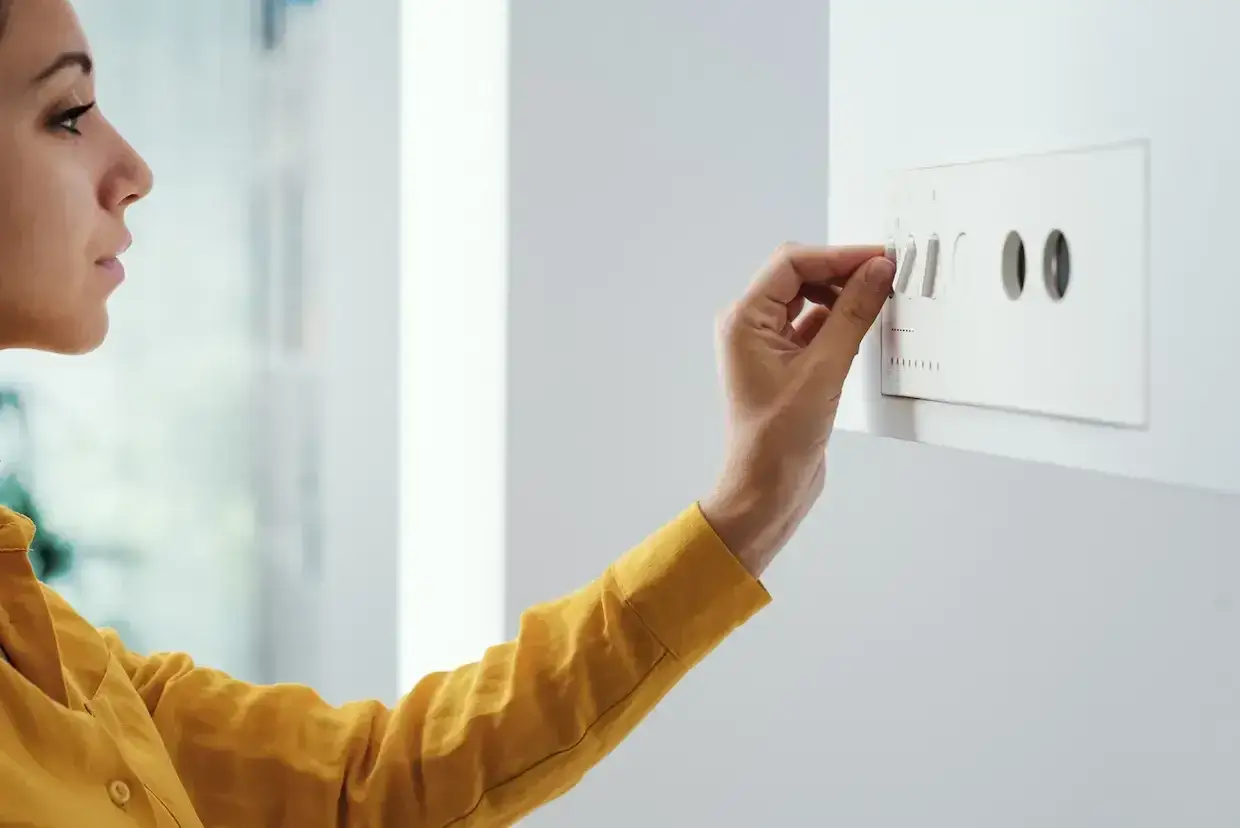 Une femme ajuste un thermostat, une action simple pour red&eacute;marrer une chaudi&egrave;re en s&eacute;curit&eacute; et assurer le confort de la maison.