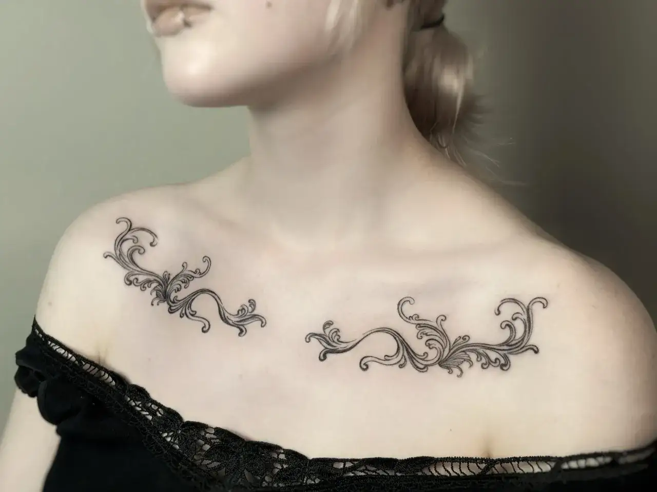 Delikatny tatuaż ornament damski na obojczykach, przypominający koronkę lub liście winorośli, dodaje subtelności.