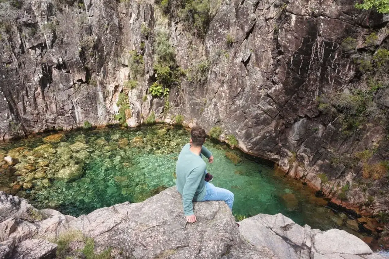 Mann sitzt auf Felsen am kristallklaren Wasser des Peneda-Gerês-Nationalparks.