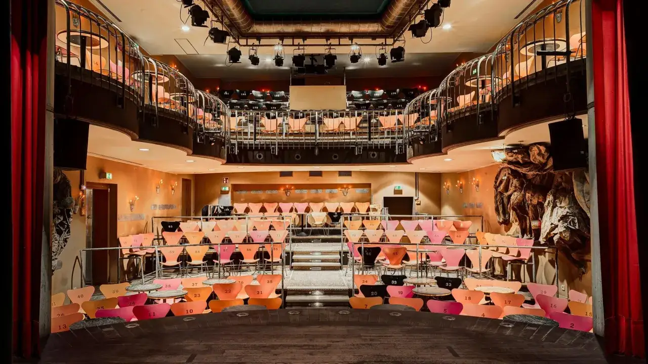 Blick in ein kleines, gem&uuml;tliches Theater mit bunten St&uuml;hlen und R&auml;ngen. Die B&uuml;hne ist leer, bereit f&uuml;r die Vorstellung im Horizont Theater.