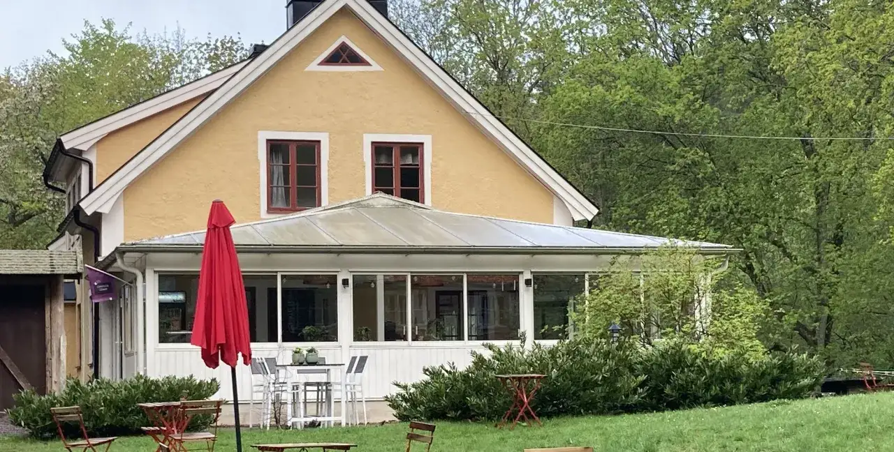 Gult hus med glasveranda och r&ouml;da parasoller. Utomhusbord och stolar i gr&auml;set. Stocklycke vandrarhem inbjuder till avkoppling.