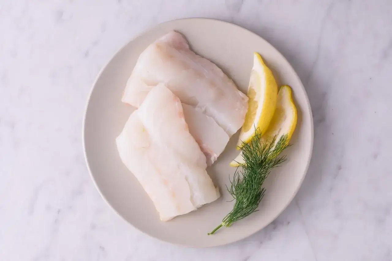 Trzy filety z dorsza, plasterki cytryny i gałązka koperku na talerzu. Niska zawartość dorsz kcal sprawia, że to zdrowy wybór.