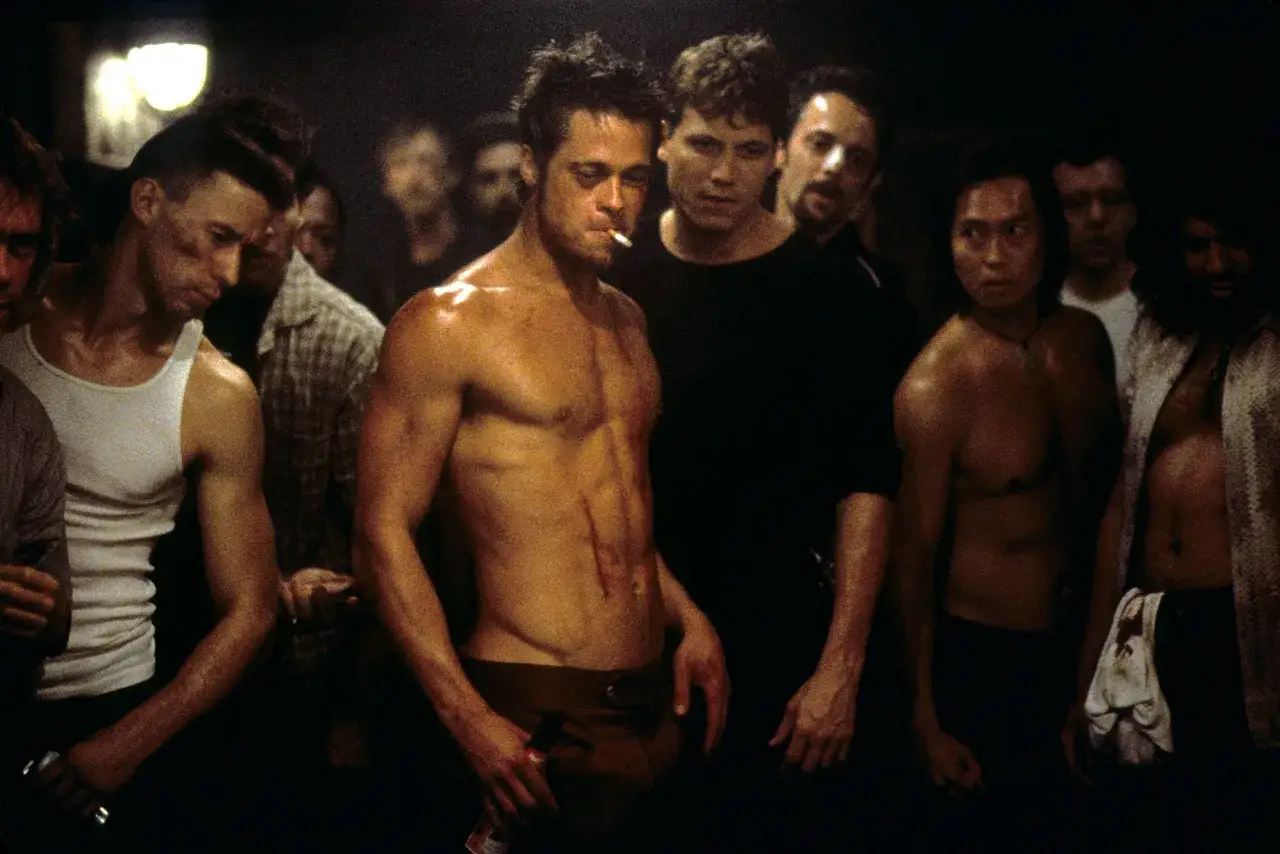 Uomini in un'oscura stanza, uno con sigaretta e addominali scolpiti, evocano il fight club significato psicologico di ribellione e ricerca di identità.